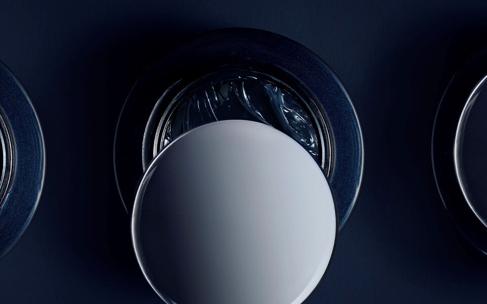 Open Biotherm skincare jar viewed from above, showing swirl of dark cream inside under soft lighting.