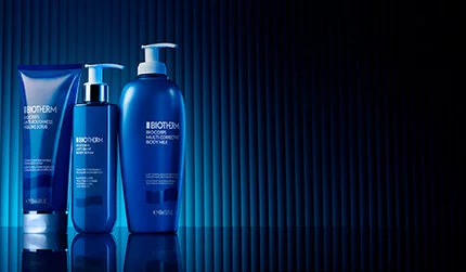 Three Biotherm dark blue bottles of body care range, set against a textured vertical striped background with dramatic lighting.
