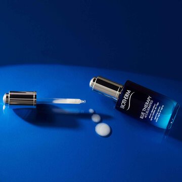 Open Biotherm Blue Therapy serum bottle with dropper and white liquid on glossy blue surface.
